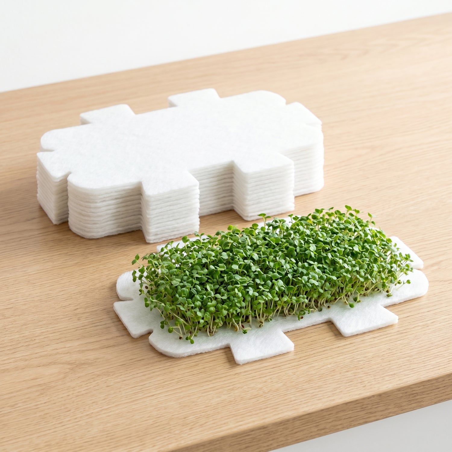 Stack of LaNiTex microgreen growing mats - soil-free polyester fibre pads with fresh microgreens sprouting on one mat
