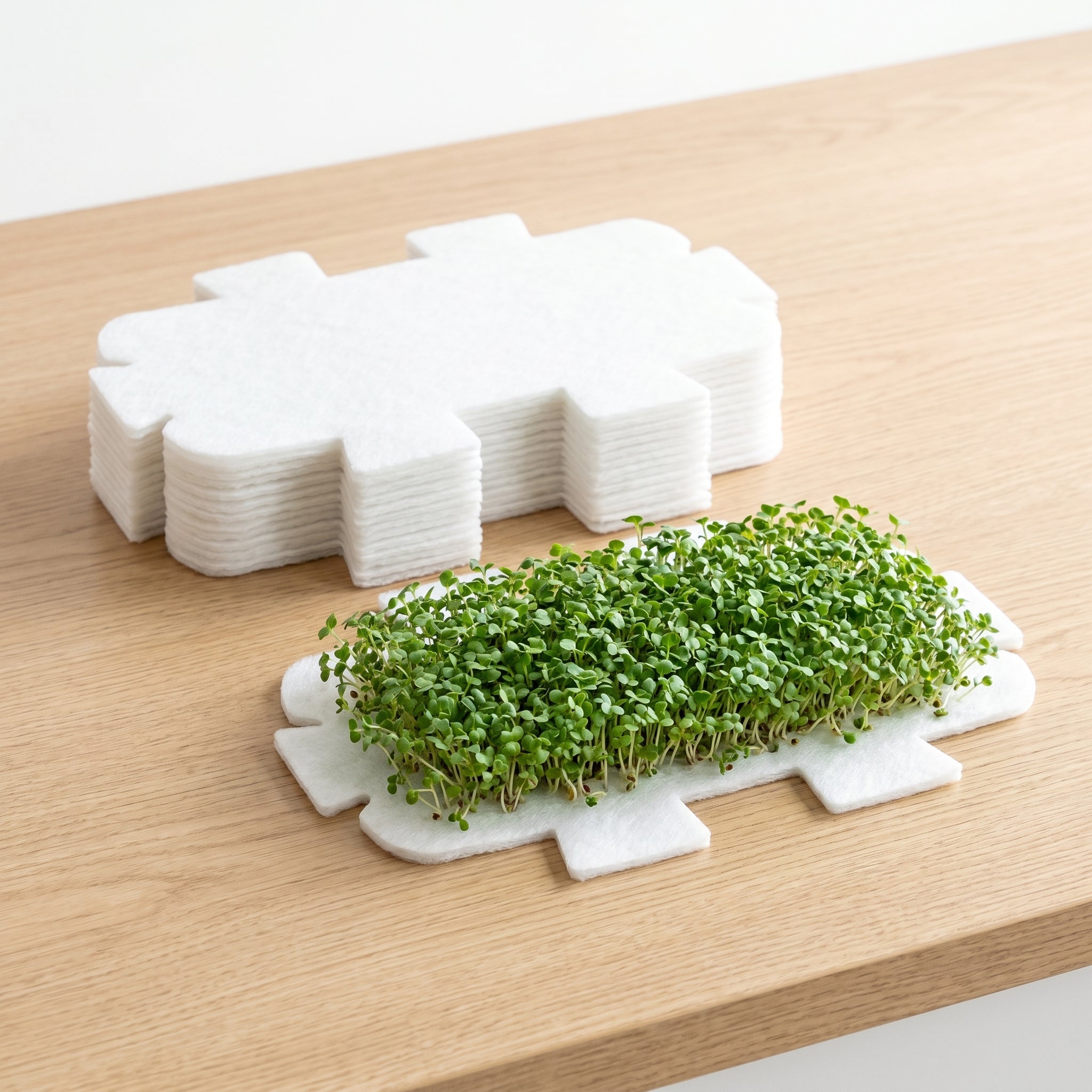 Stack of LaNiTex microgreen growing mats - soil-free polyester fibre pads with fresh microgreens sprouting on one mat