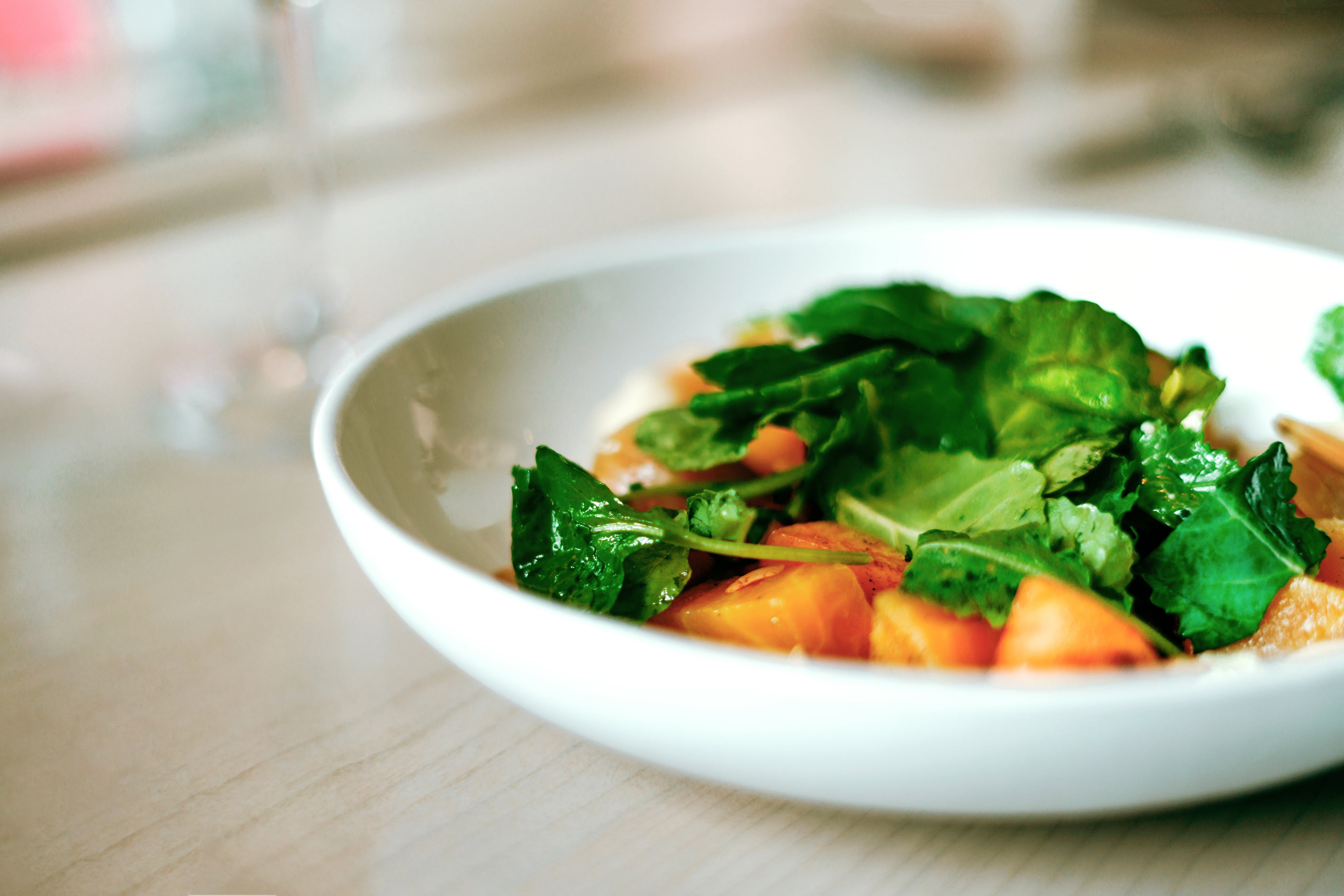 A fresh salad with leafy greens, carrot slices, and possibly sweet potatoes, served in a bowl on a wooden table.