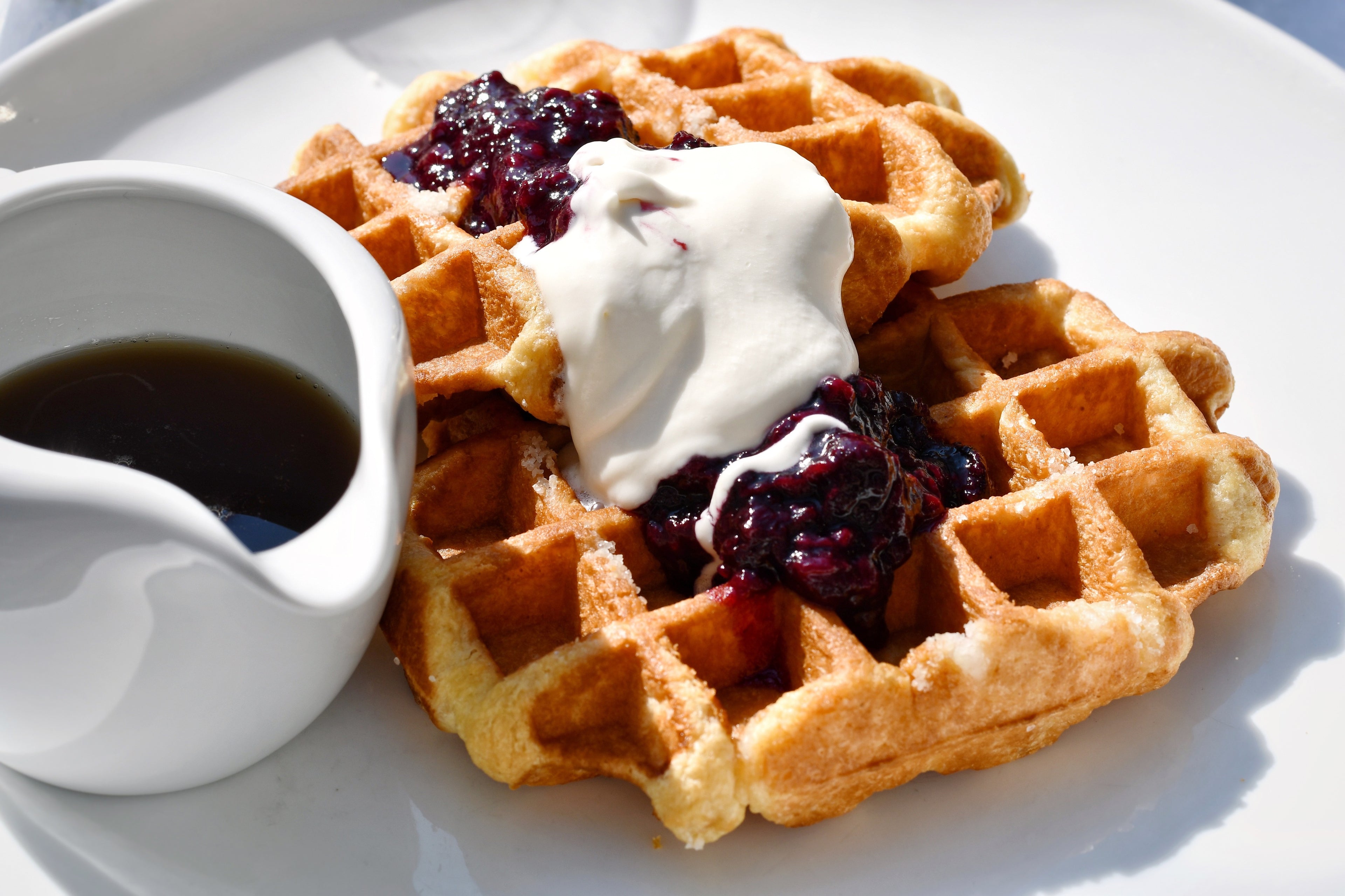 Golden-brown waffles topped with a dollop of cream and vibrant red jam